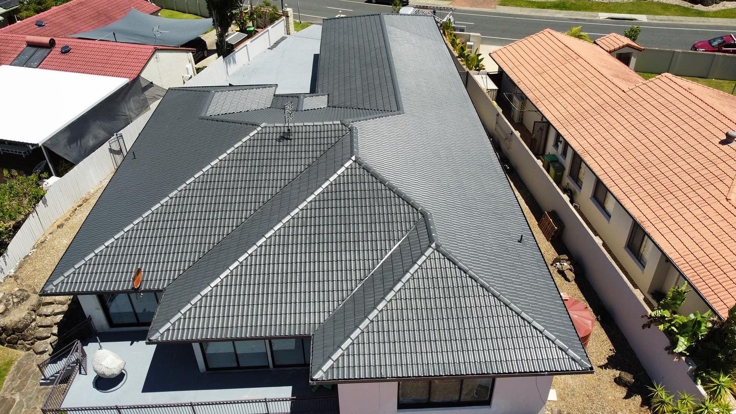 Overhead view of a house with a dark gray tiled roof, surrounded by other houses and a street. - Roof Painting in Gold Coast,QLD