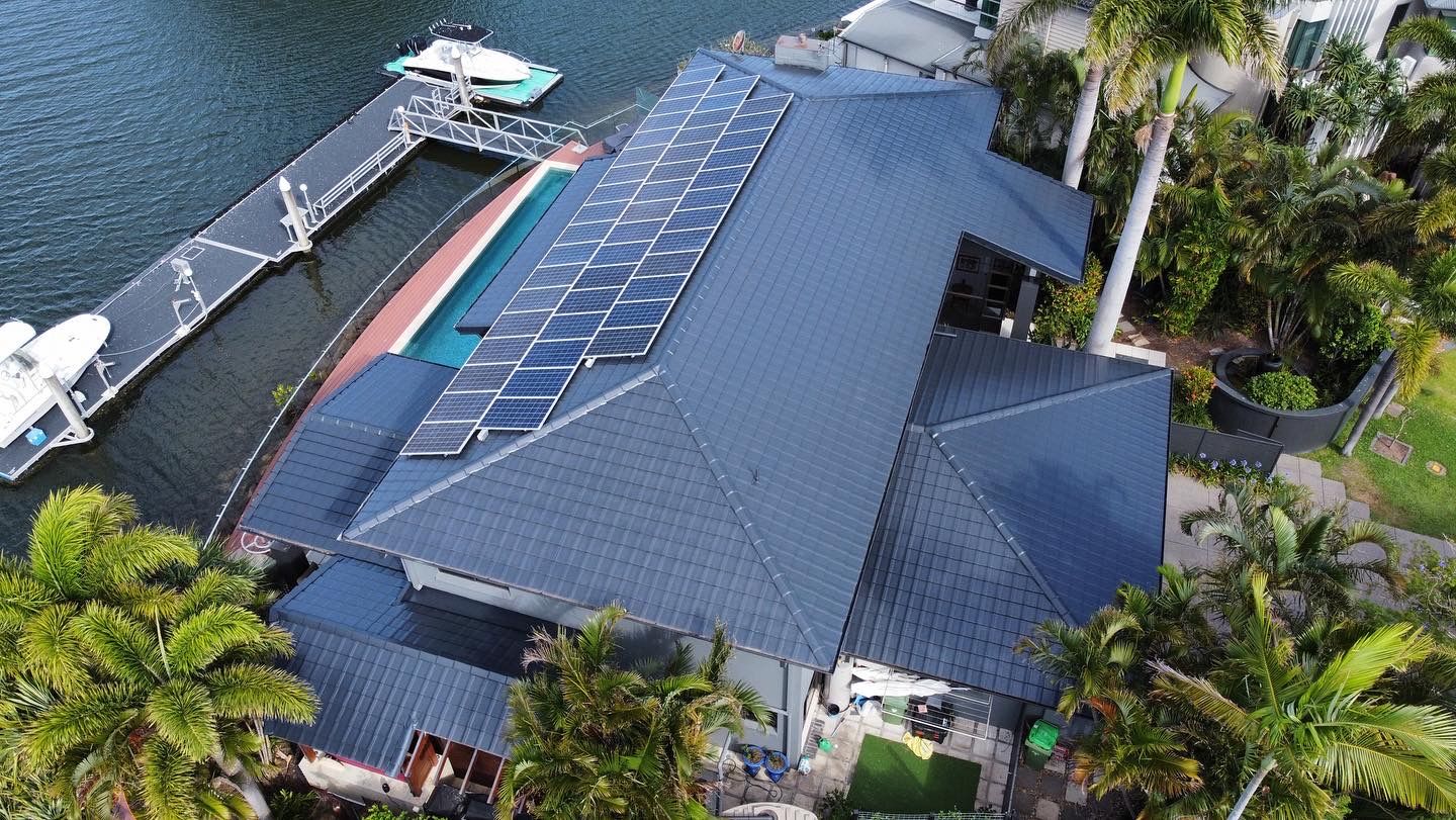 Aerial view of a house with solar panels on the roof next to a dock with boats on a canal. - Roof Painting in Gold Coast,QLD