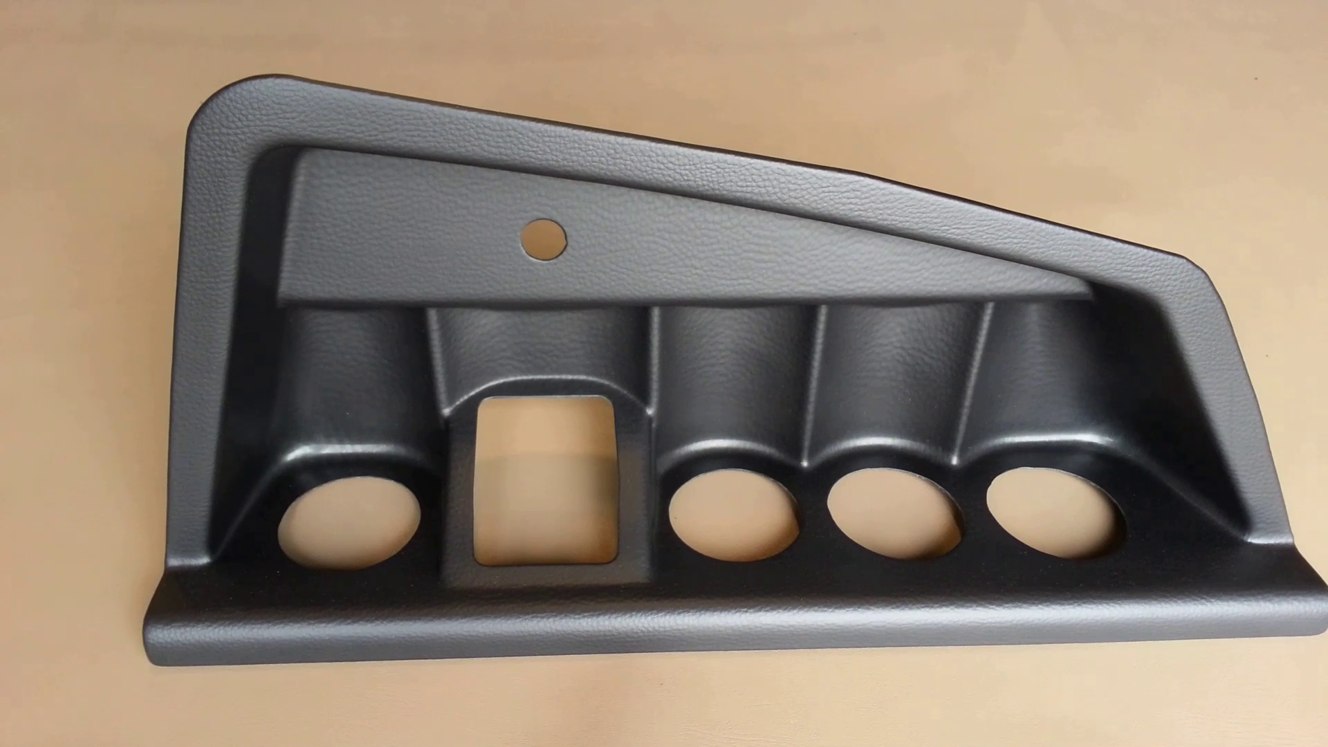 Black molded plastic trim panel with four circular cutouts