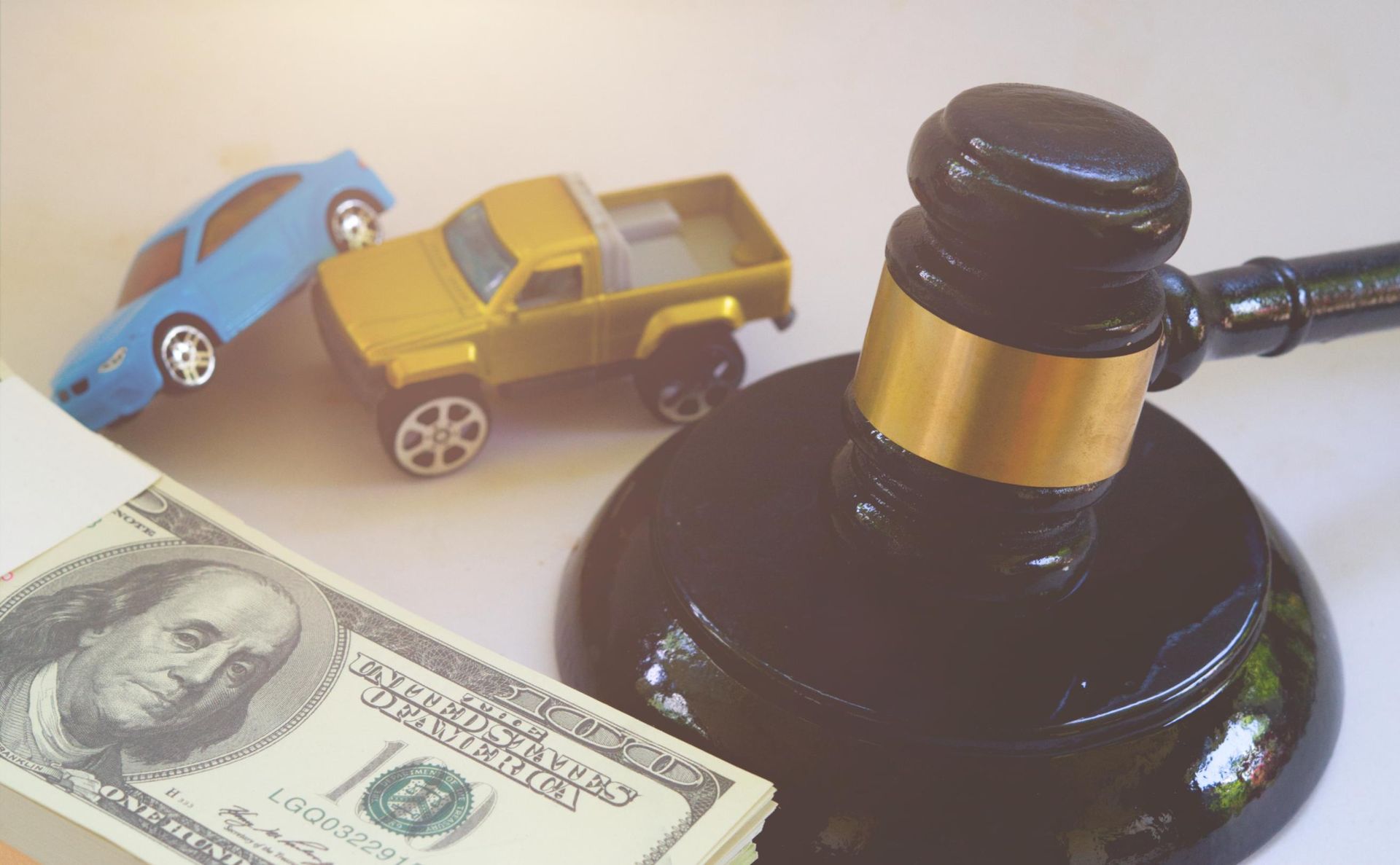 Toy car crash beside judge’s gavel and $100 bill, symbolizing an auto accident claim or lawsuit