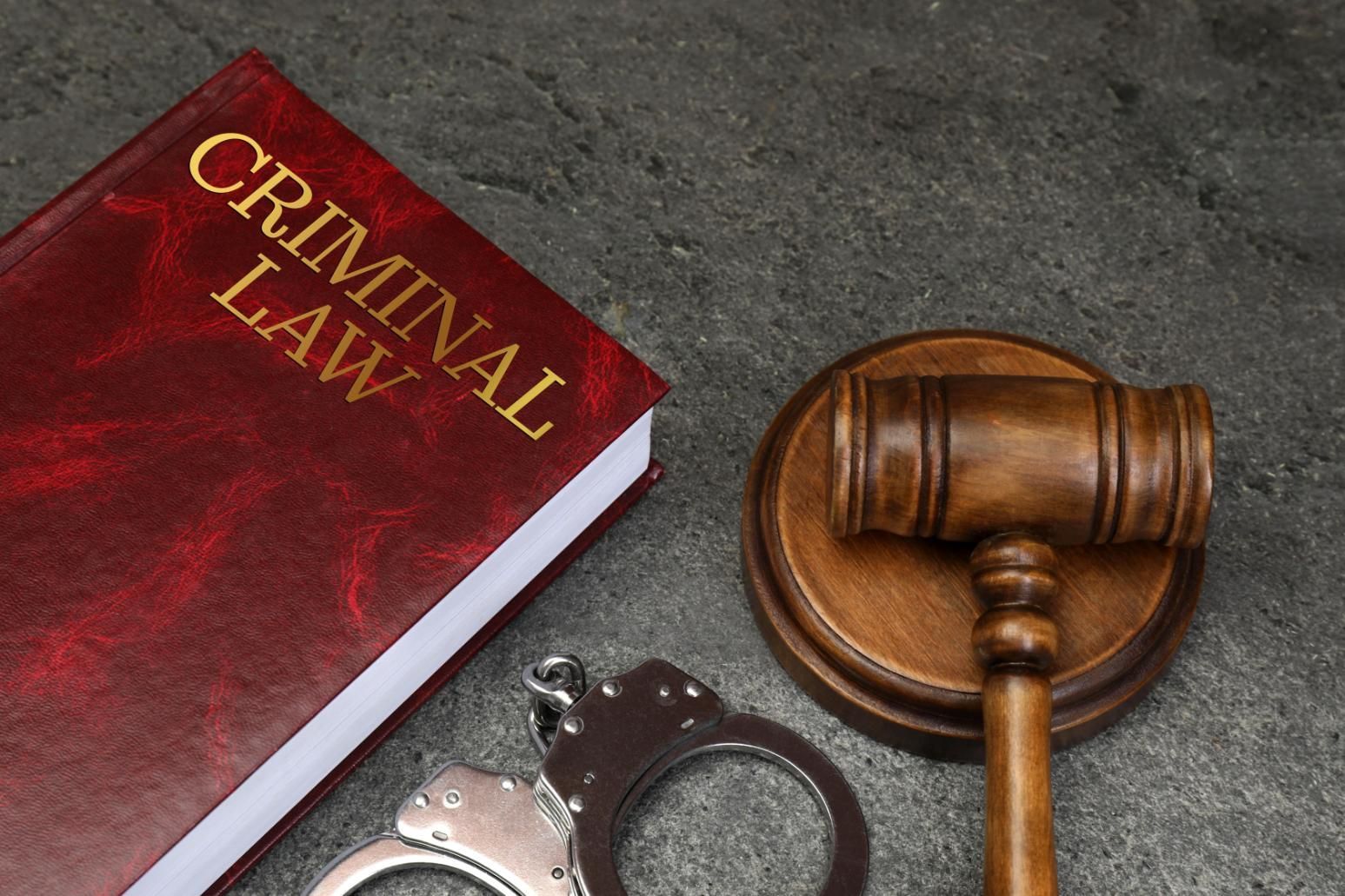 Criminal law book, handcuffs, and a judge’s gavel on a gray surface