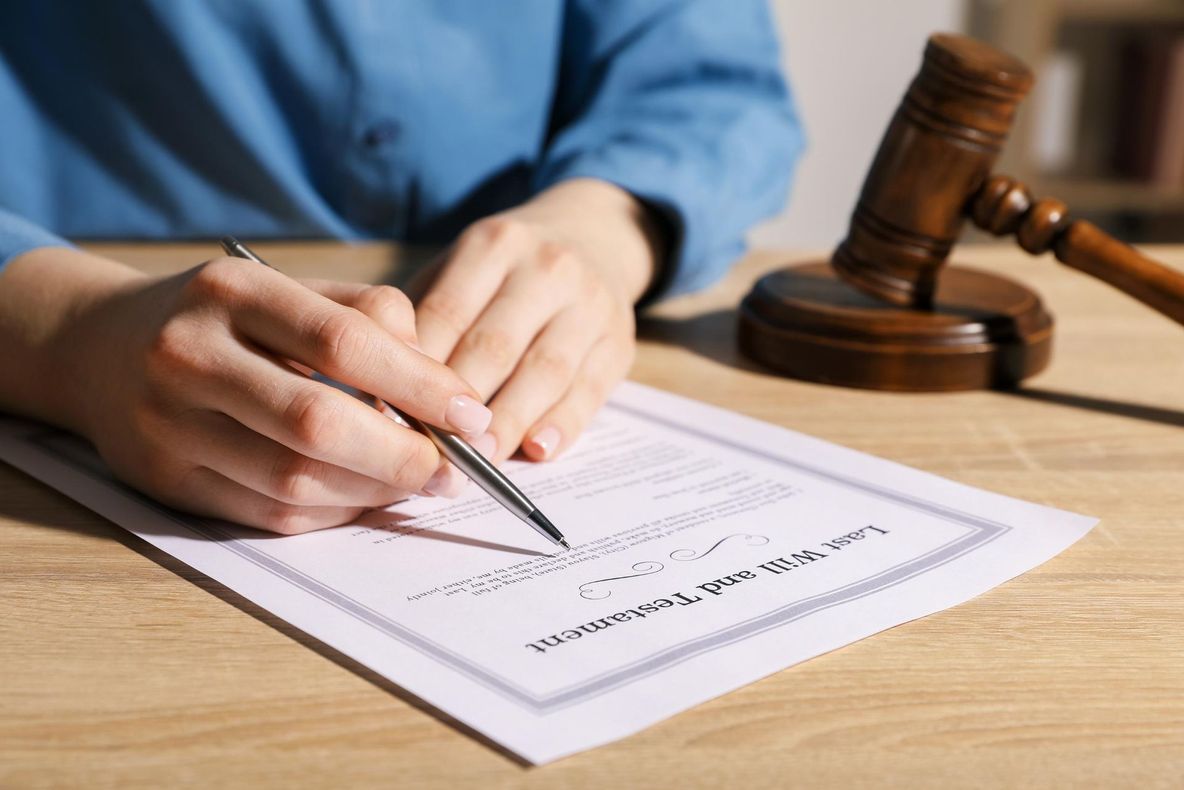 Hand signing a document on a wooden desk beside a judge’s gavel