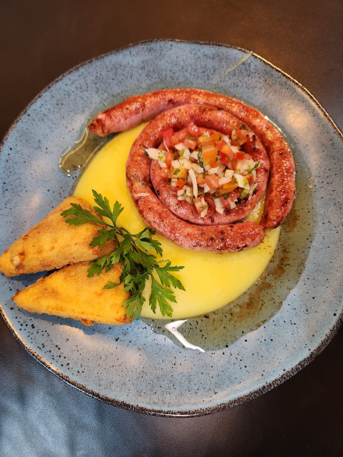 Um prato de comida com uma salsicha e purê de batatas sobre uma mesa.