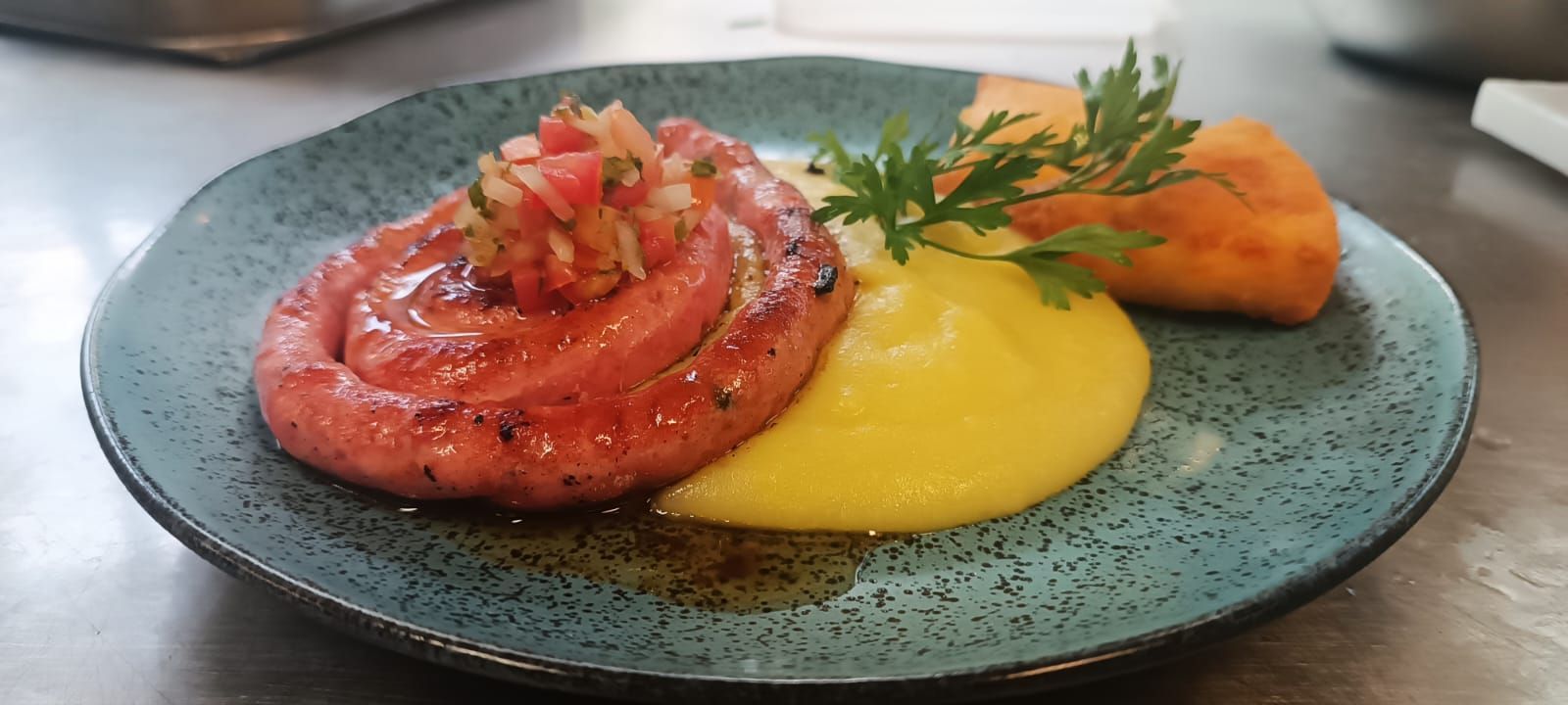 Um prato de comida com uma salsicha e purê de batatas sobre uma mesa.