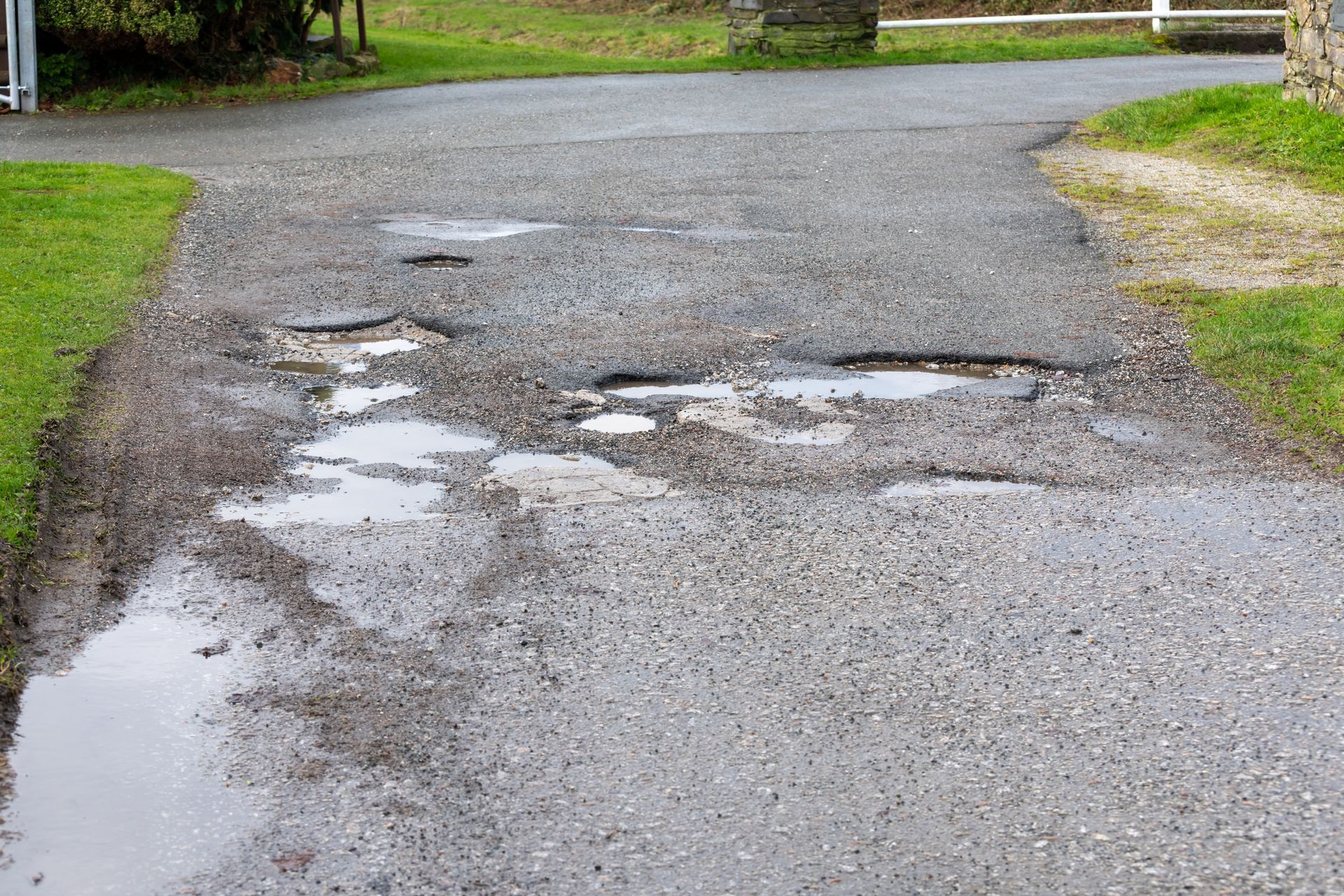 Driveway pothole with standing water on a damaged asphalt driveway