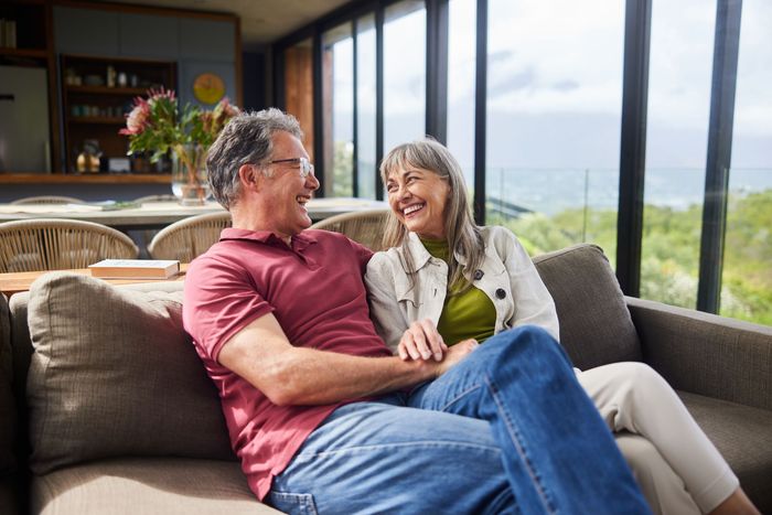 Couple smiling on a sofa in a bright living room with a large window and outdoor view