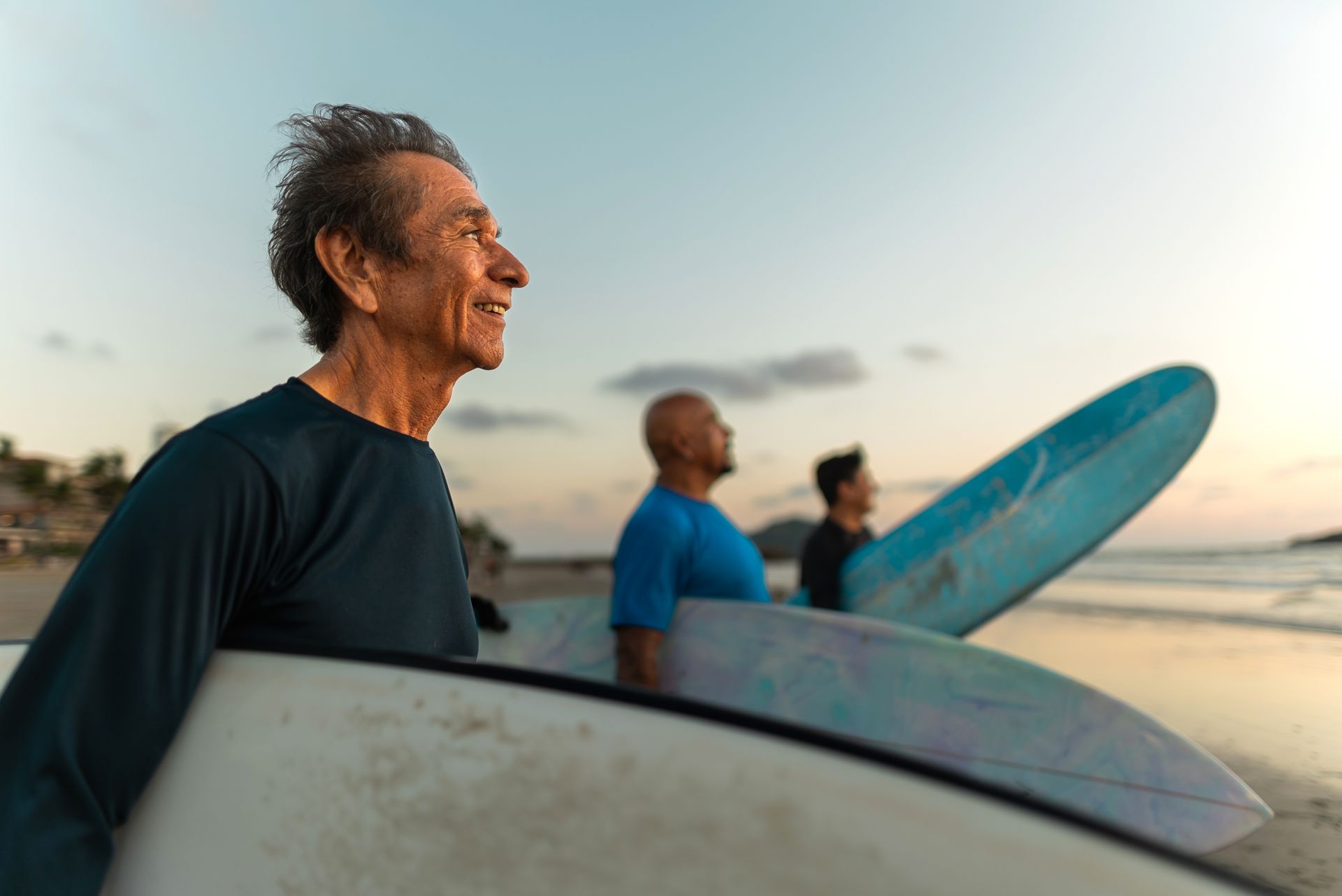 Surfers holding surfboards at the beach during sunset