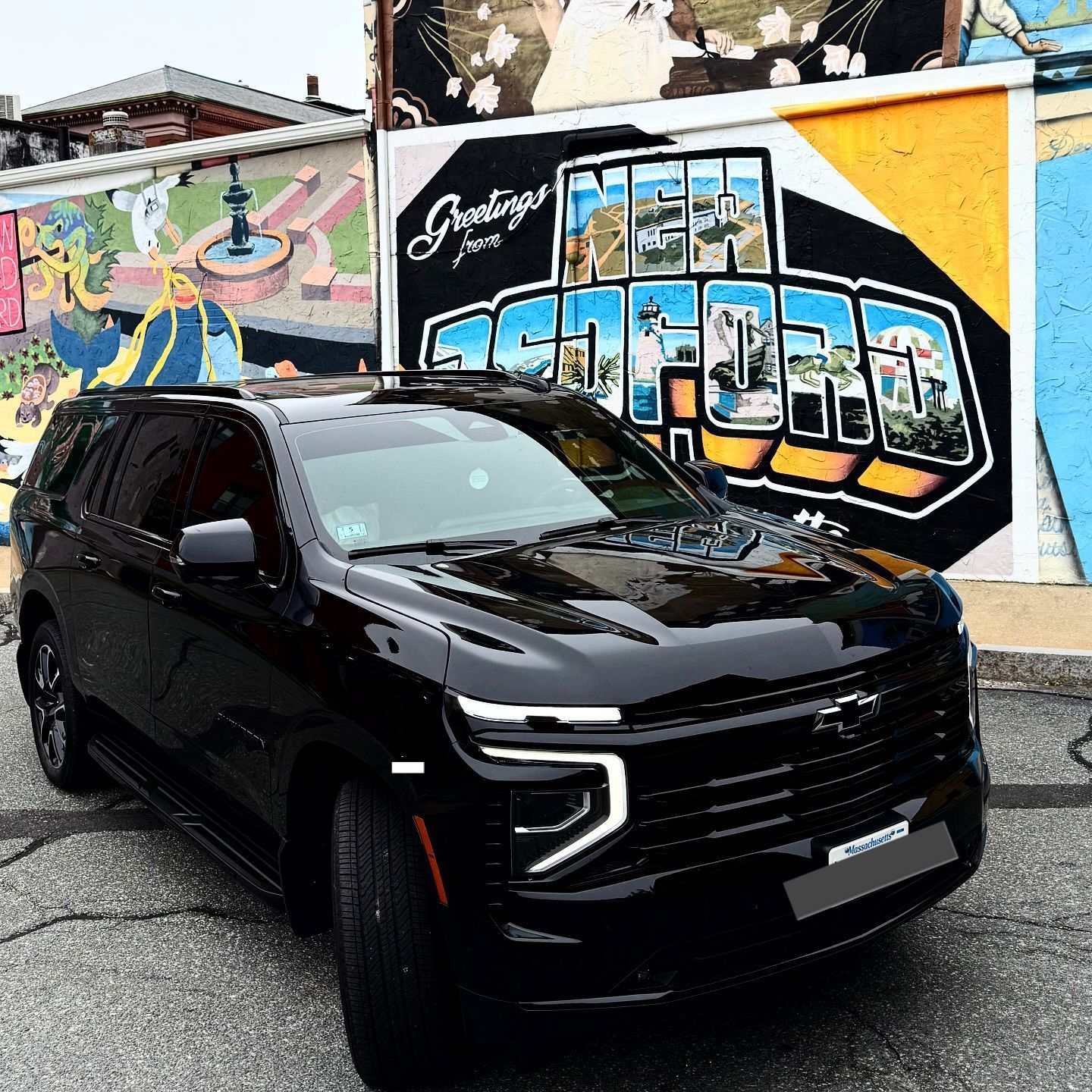 Black SUV parked in front of a colorful graffiti mural on a city street