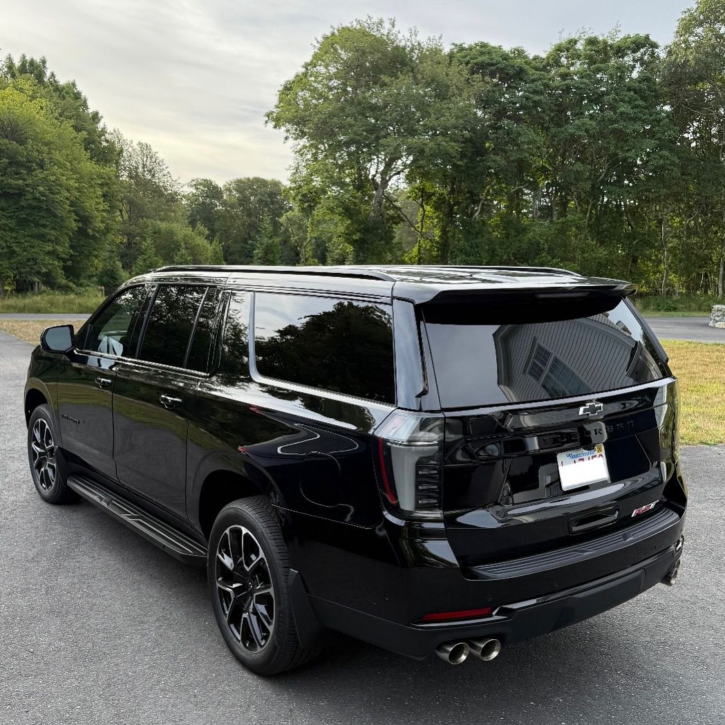 Black SUV parked on a road beside trees and grass, viewed from the rear side.