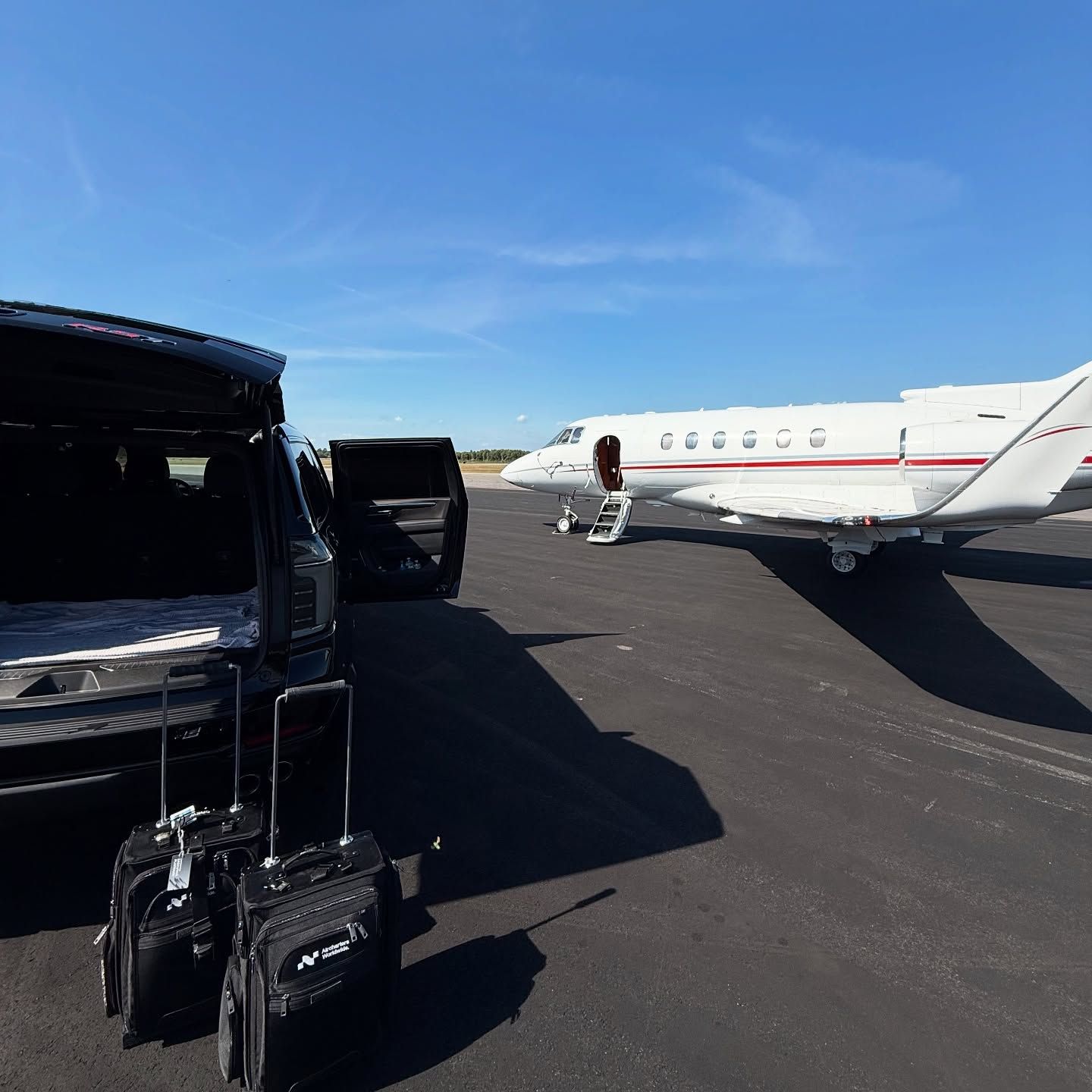 Black private jet on tarmac with luggage carts beside it under a clear blue sky