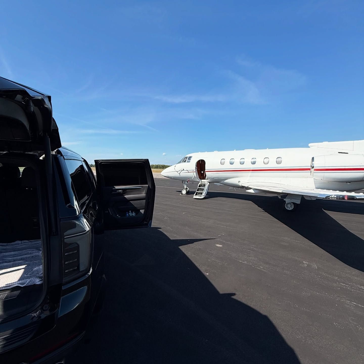 Private jet parked on a runway beside an open black car under a clear blue sky
