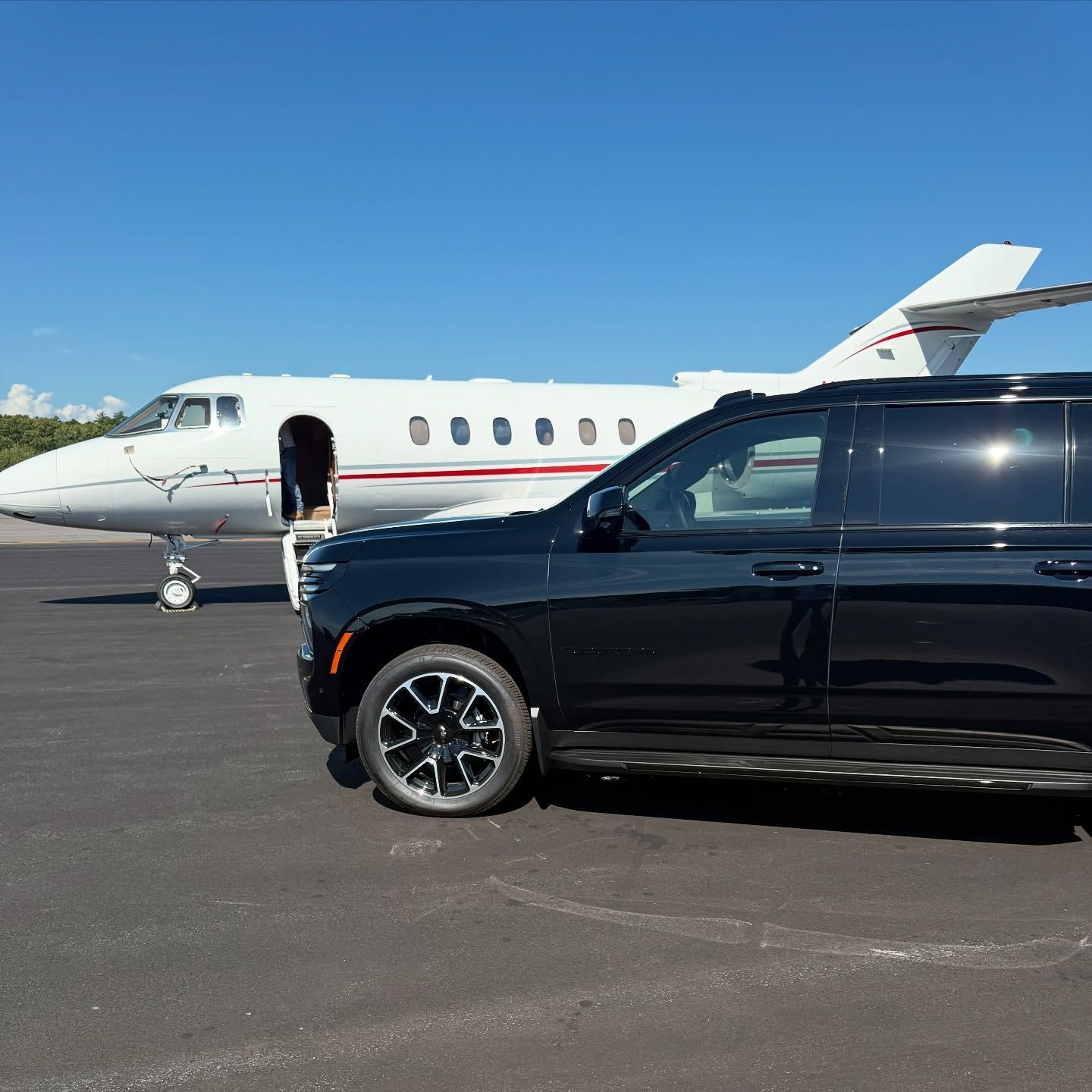 Black SUV in front of a white private jet on a sunny airport tarmac