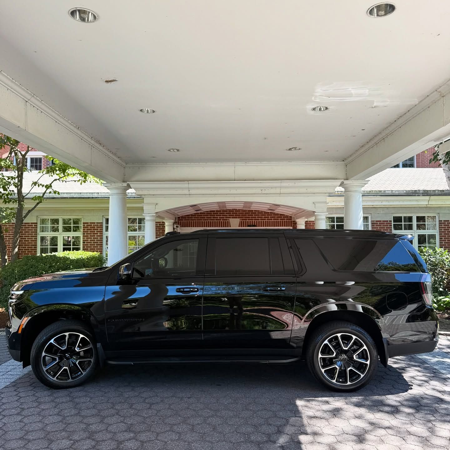 Black SUV parked under a white carport in front of a brick house