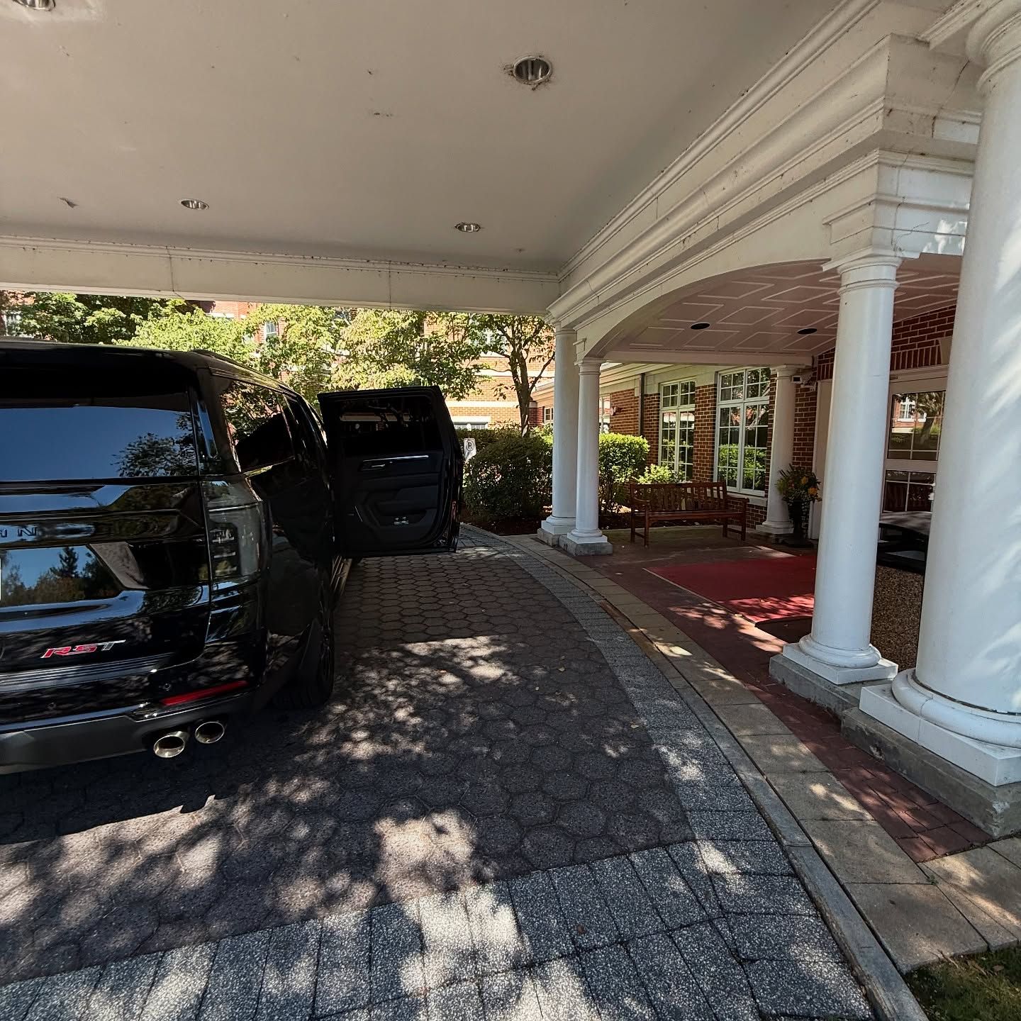Covered driveway with black SUVs parked beside white columns and a house entrance.