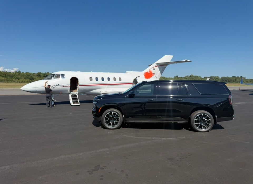 Black SUV parked beside a white private jet on an airport tarmac under clear blue sky