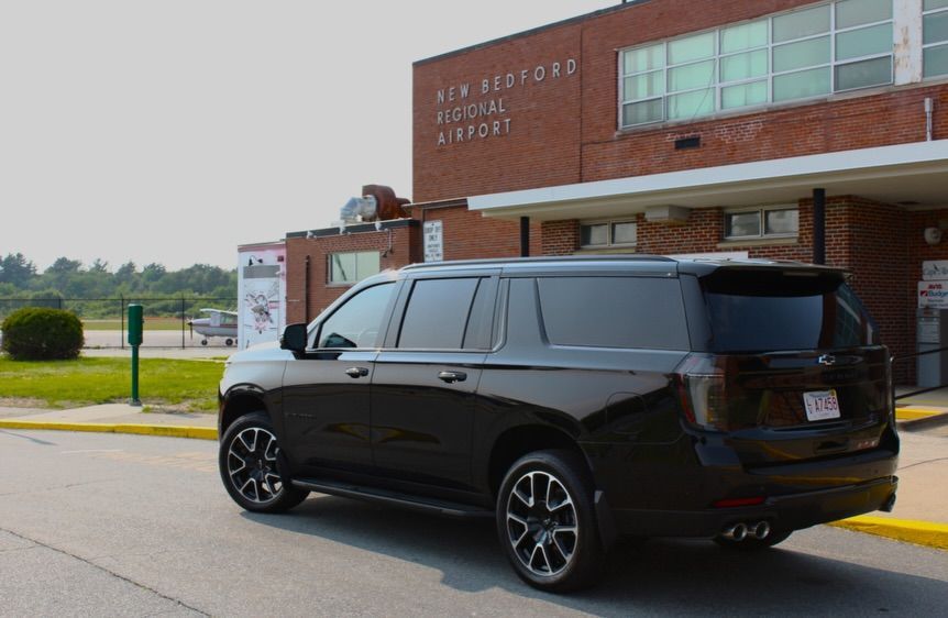 Black SUV parked outside a brick airport terminal building.