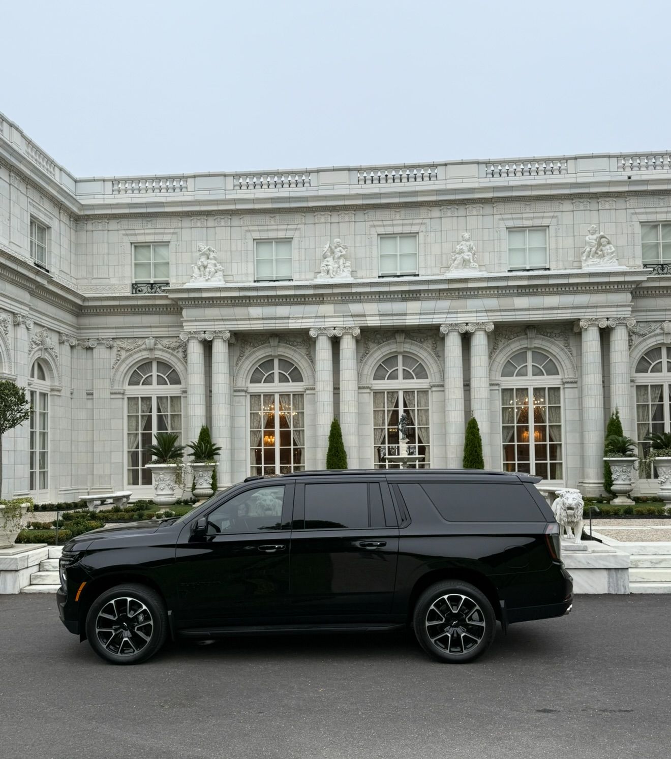 Black SUV parked in front of a grand white mansion with columns and large windows