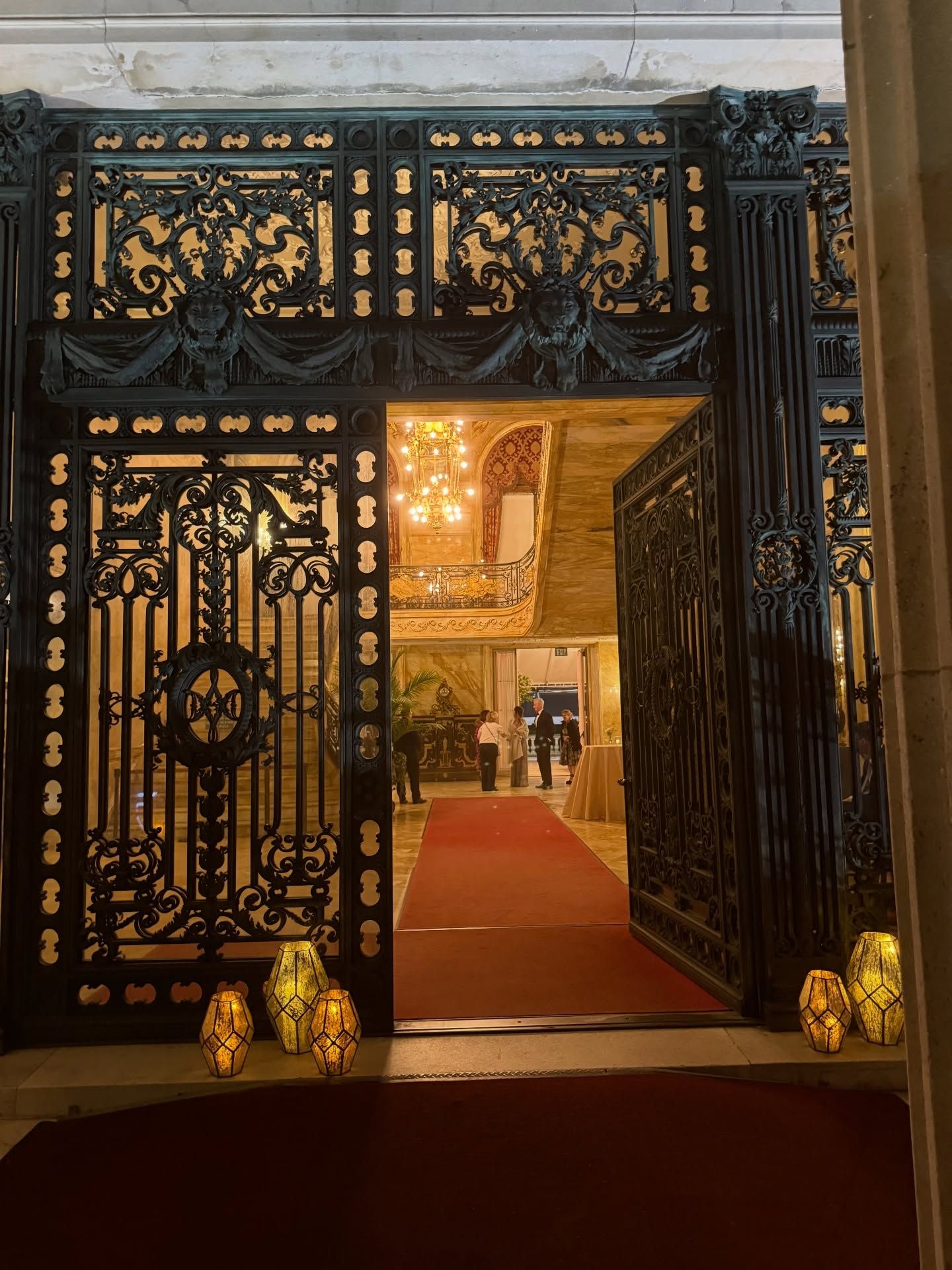 Ornate black and gold gate opening to a red-carpeted interior with warm lights