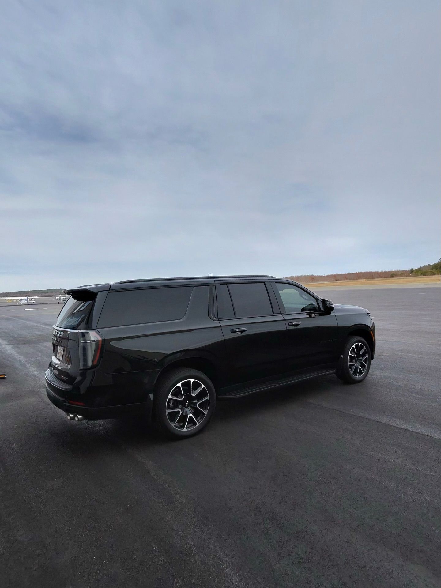 Black SUV parked on a wet road under a cloudy sky near an open, barren shoreline.