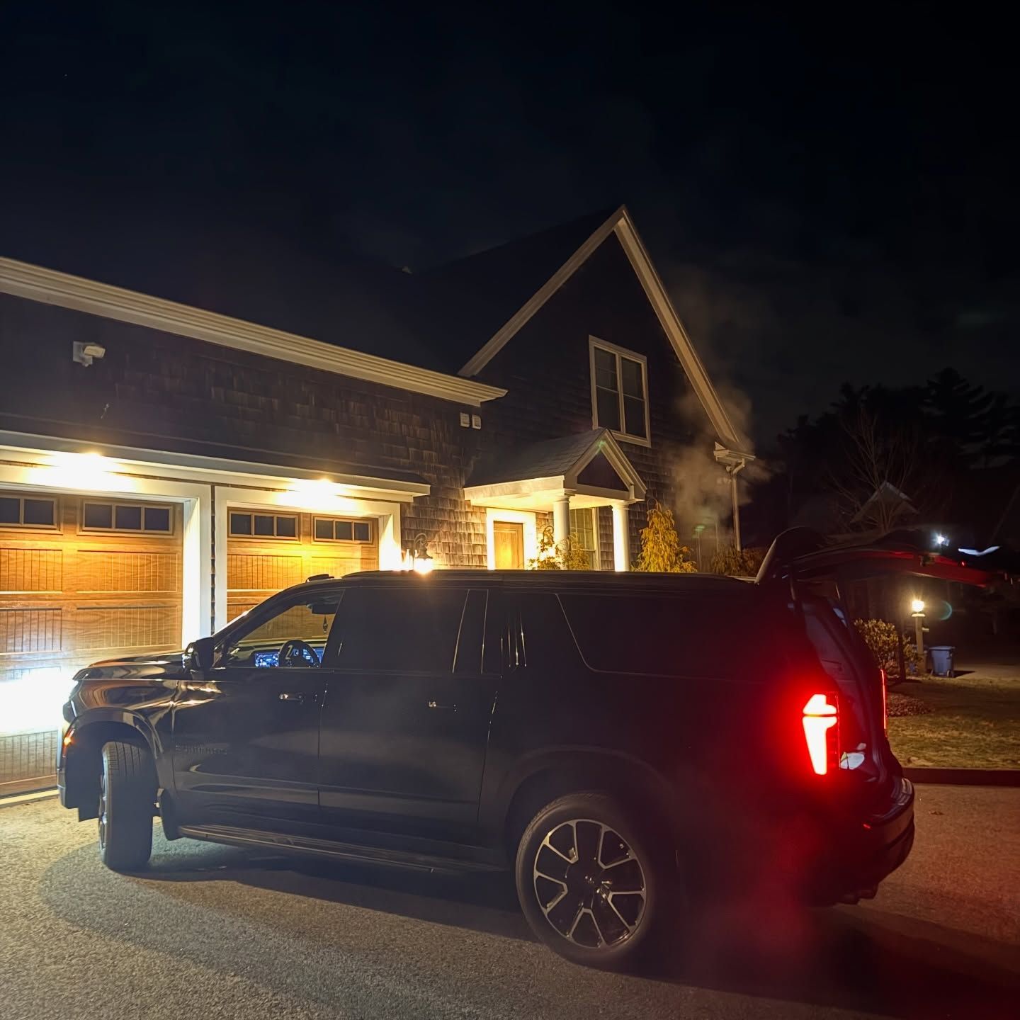Black SUV parked in front of a lit suburban house at night