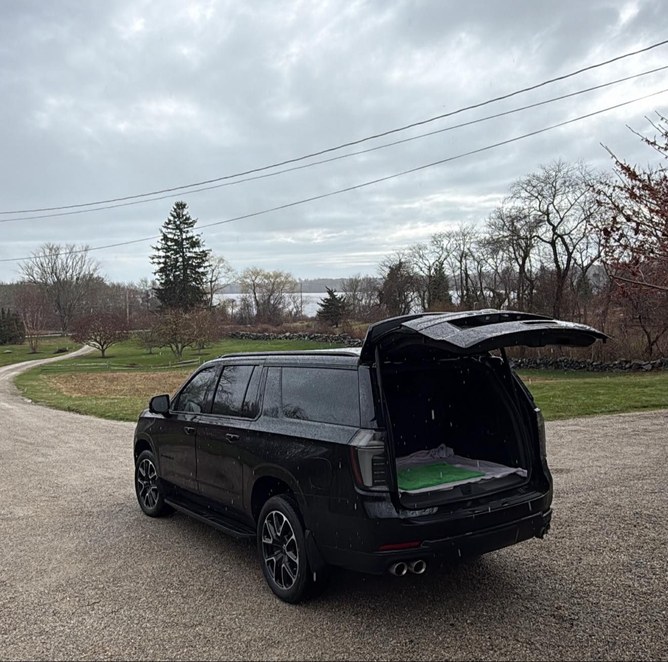 Black SUV with rear hatch open on a gravel road in a cloudy rural area