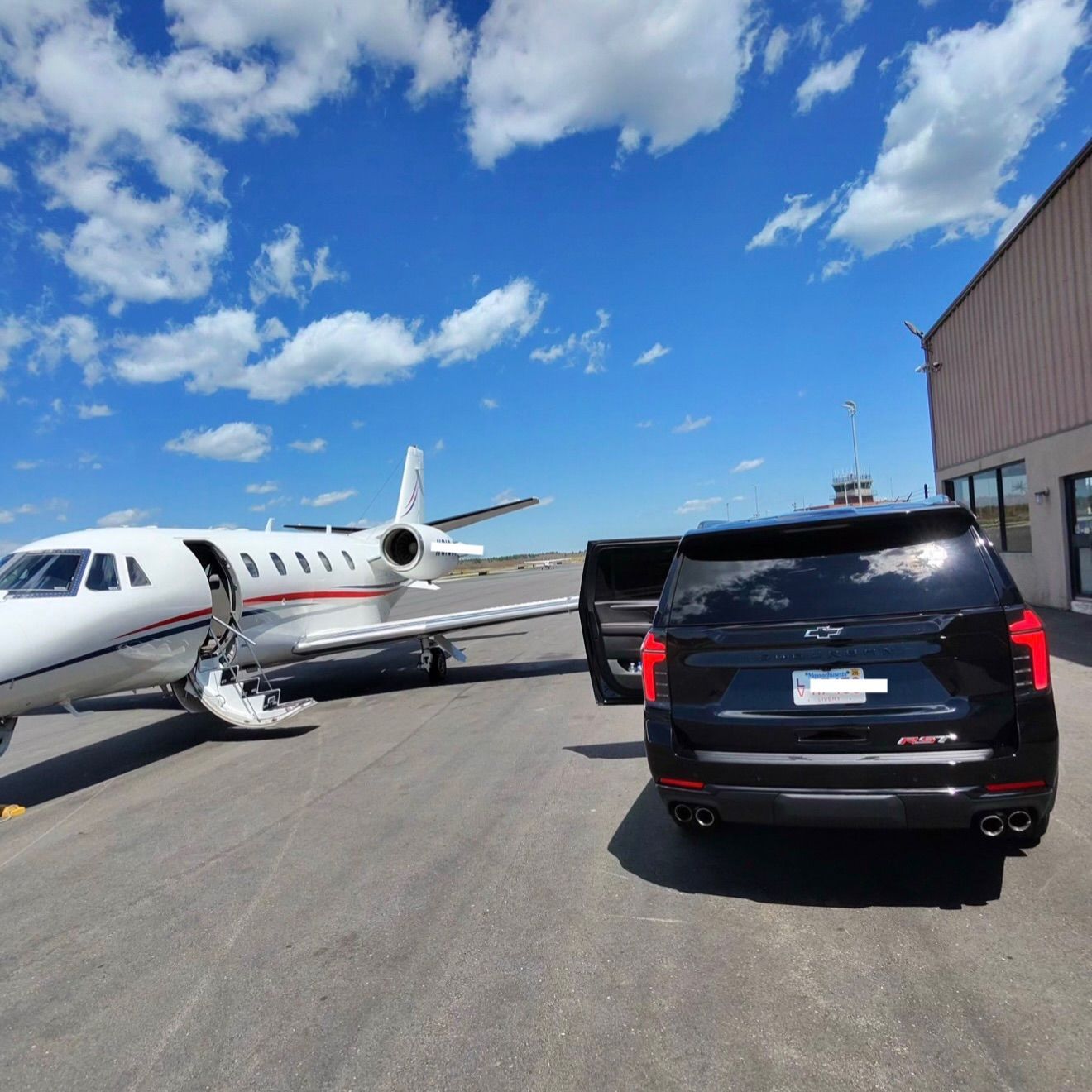 Private jet parked on an airport tarmac beside black SUVs under a bright blue sky.