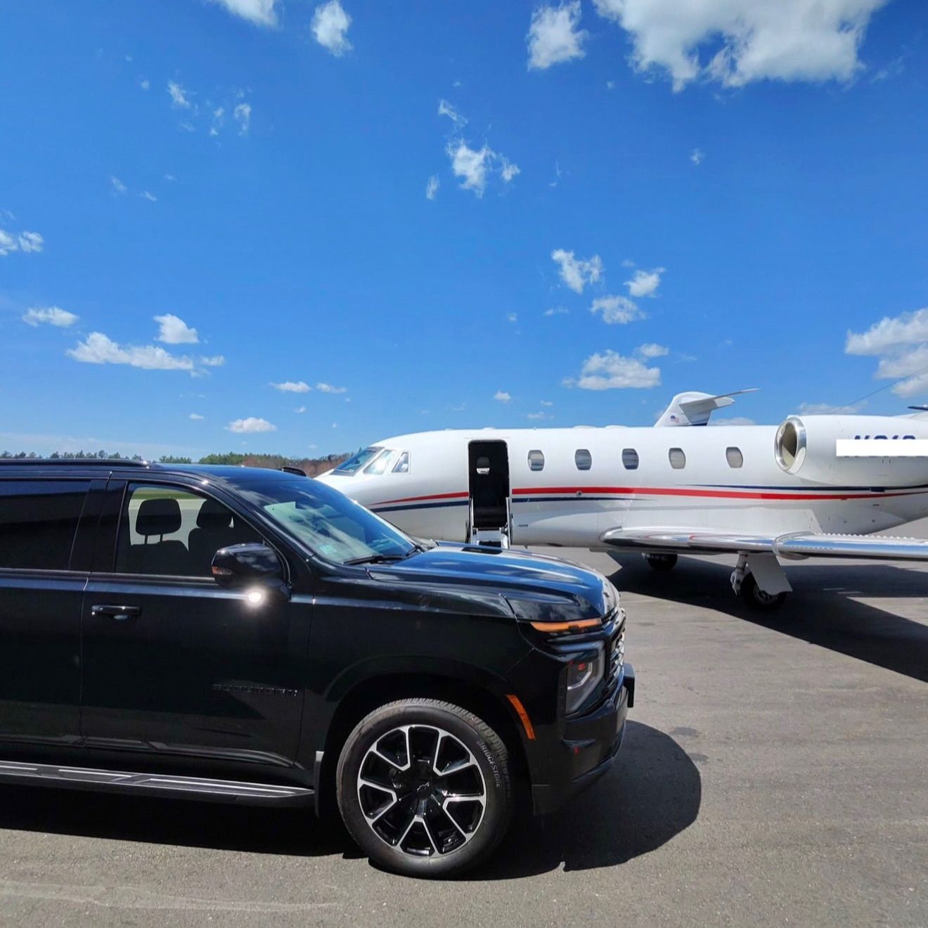Black SUV parked on tarmac beside a white private jet under a blue sky