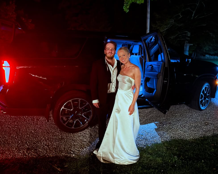 Bride in a wedding dress and veil sits in a car holding a bouquet.