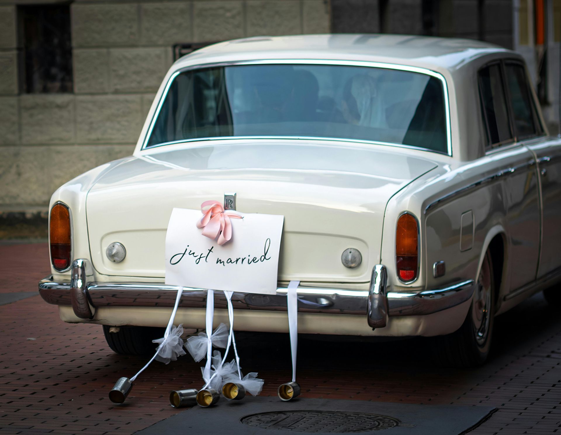 White vintage car decorated for a wedding with a floral sign hanging on the rear bumper
