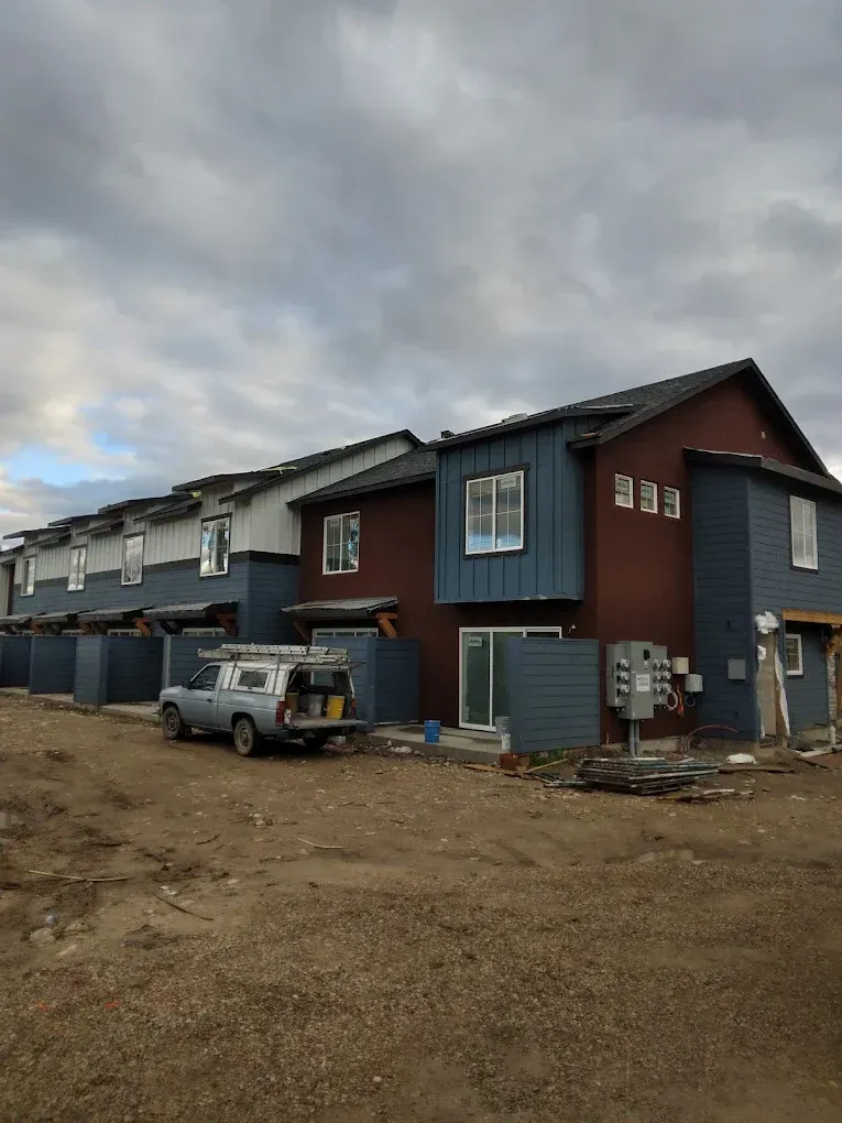 Row of modern townhouses under cloudy sky, with a truck parked on muddy construction ground