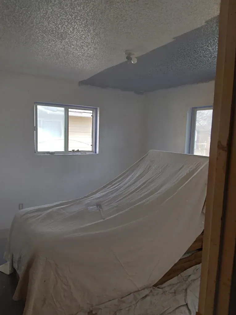 Small room with a draped couch or bed frame under white sheets, two windows, and blue-gray walls.