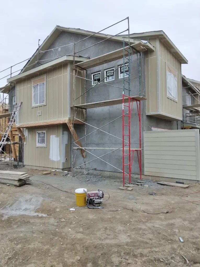 Two-story house under construction with scaffolding, unfinished siding, and bare dirt yard