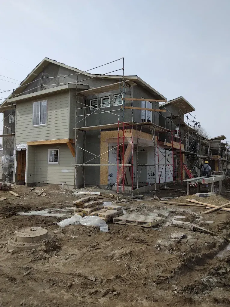 Partially built two-story house with scaffolding and exposed framing on a muddy construction site