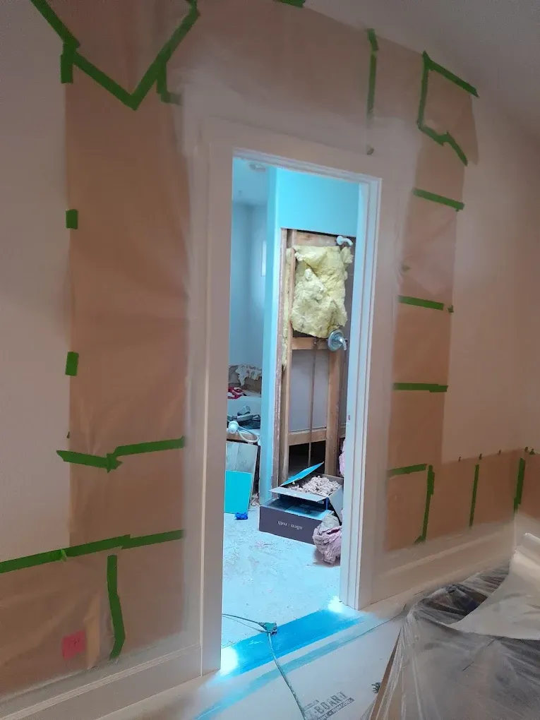 Masked doorway in a room under renovation, with taped-off walls and debris on the floor.