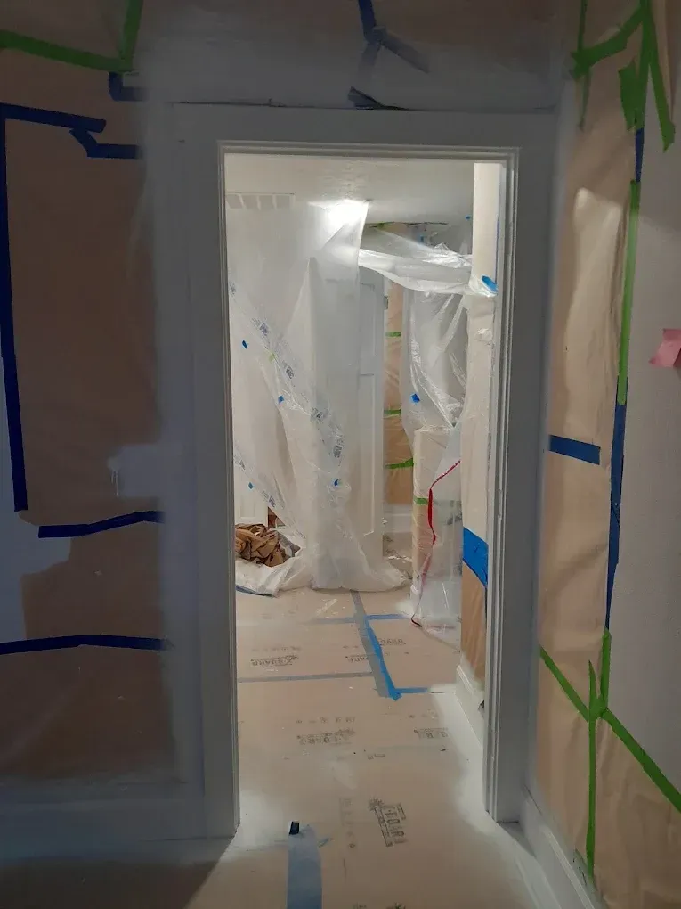 Plastic-covered hallway with blue painter’s tape and a doorway leading into a renovated room.