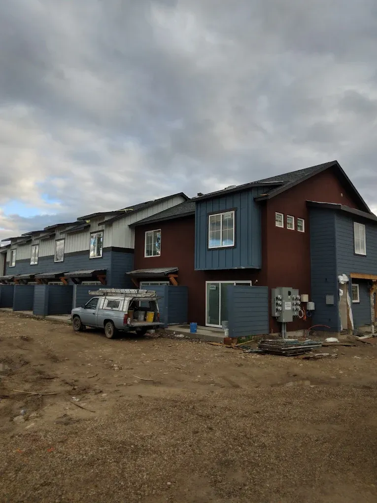 Row of modern townhouses under cloudy sky, with a truck parked on muddy construction ground
