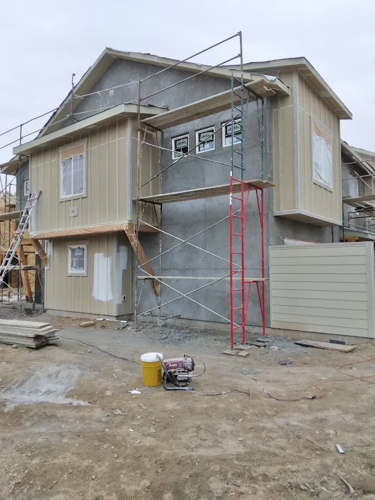 Two-story house under construction with scaffolding, unfinished siding, and bare dirt yard