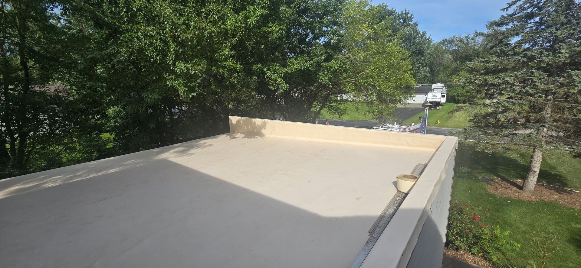 Flat white rooftop surrounded by trees and greenery on a sunny day