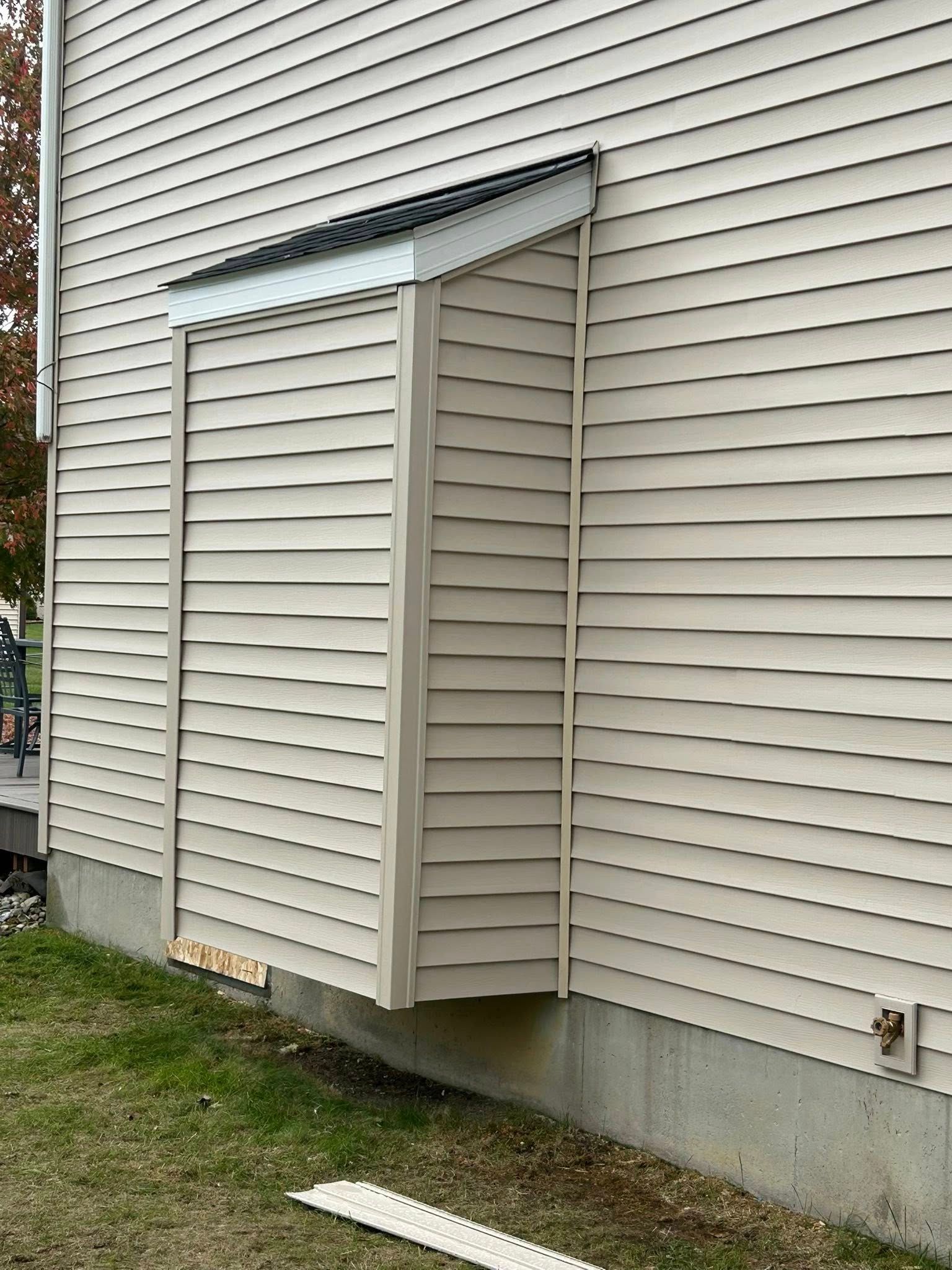 White house siding with a small exterior vent enclosure and slanted metal roof panel.