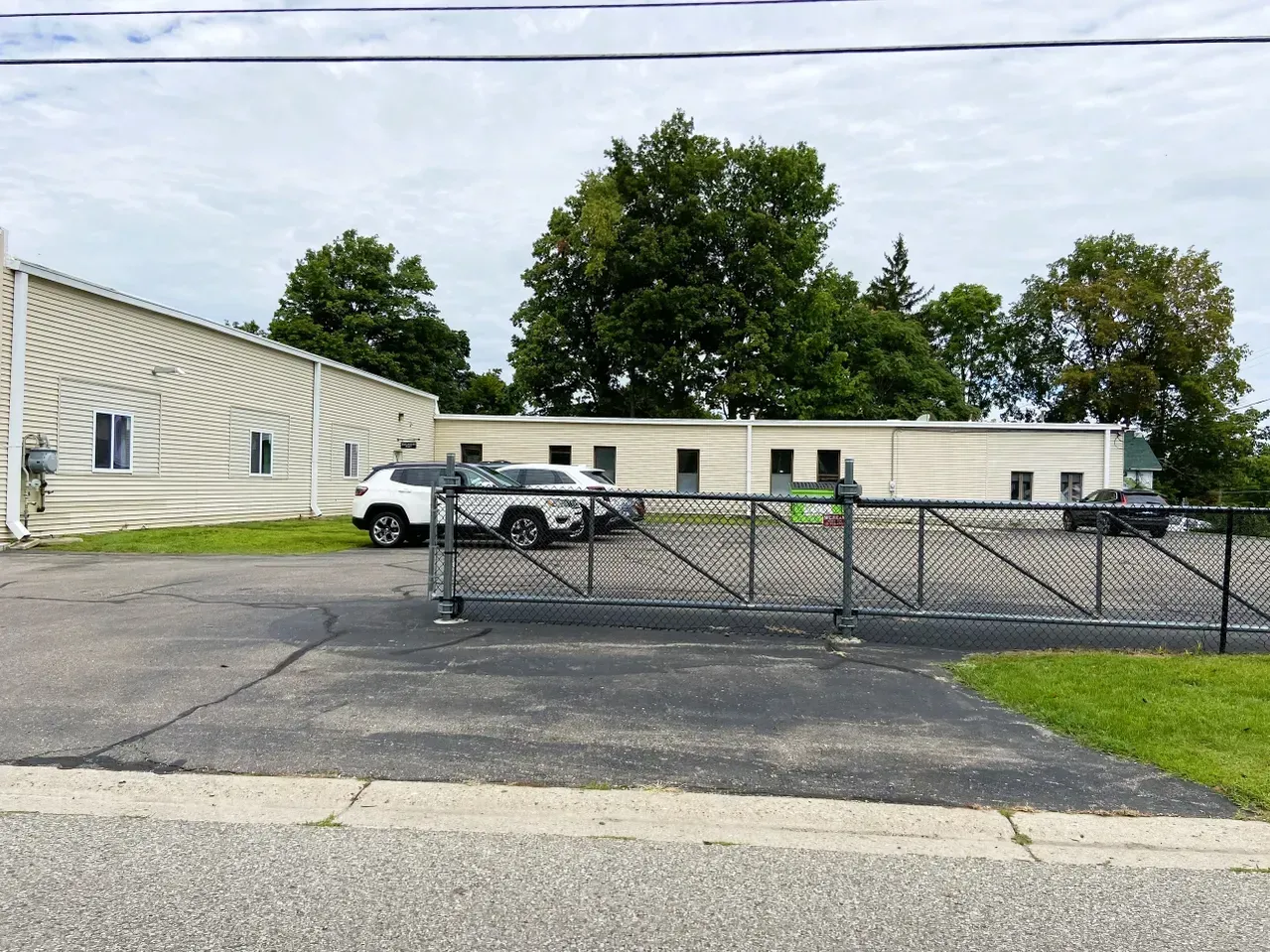 Gated parking lot beside a low beige building with several parked cars and trees in the background