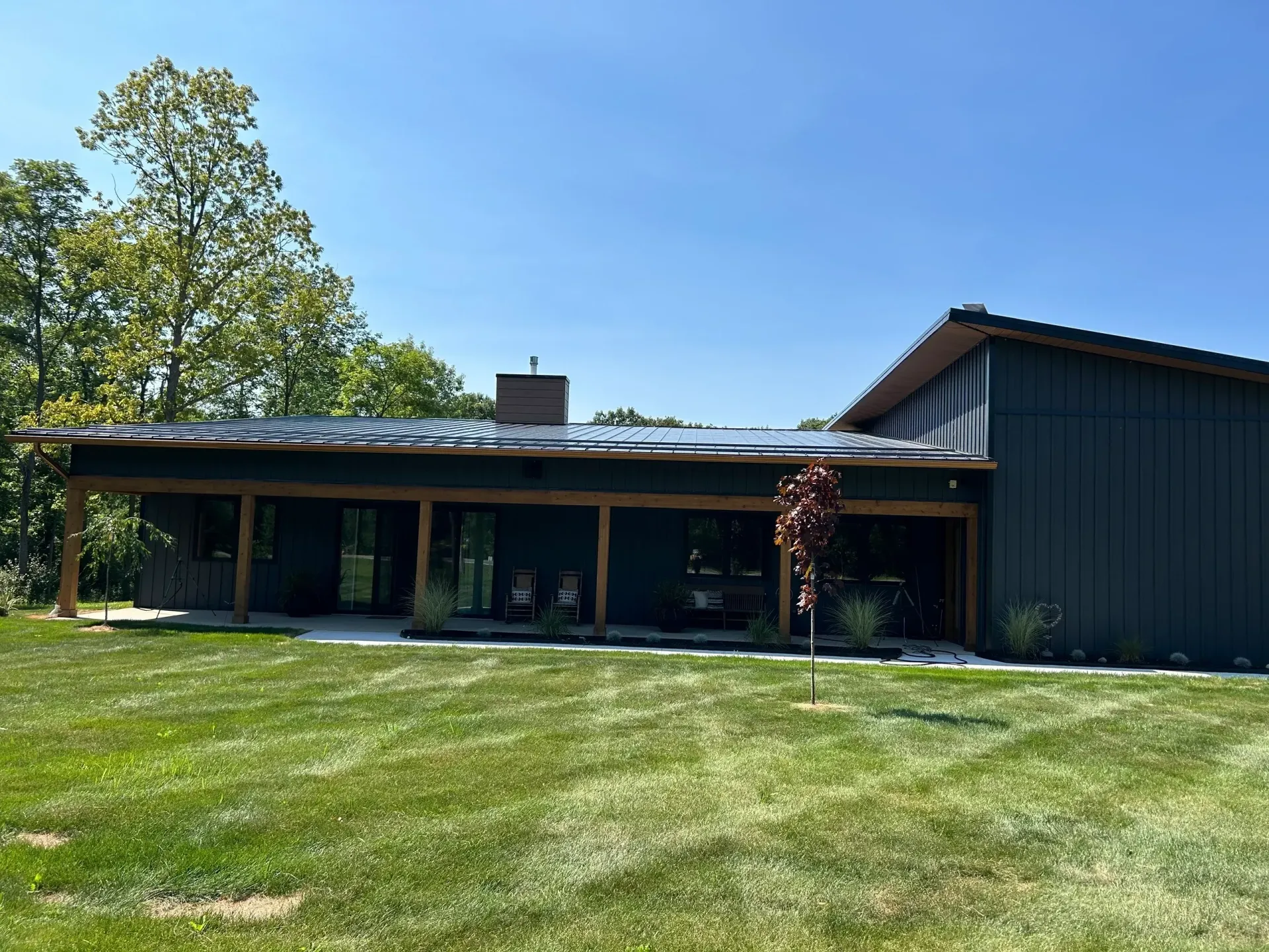 Modern black house with a covered porch and green lawn under a blue sky