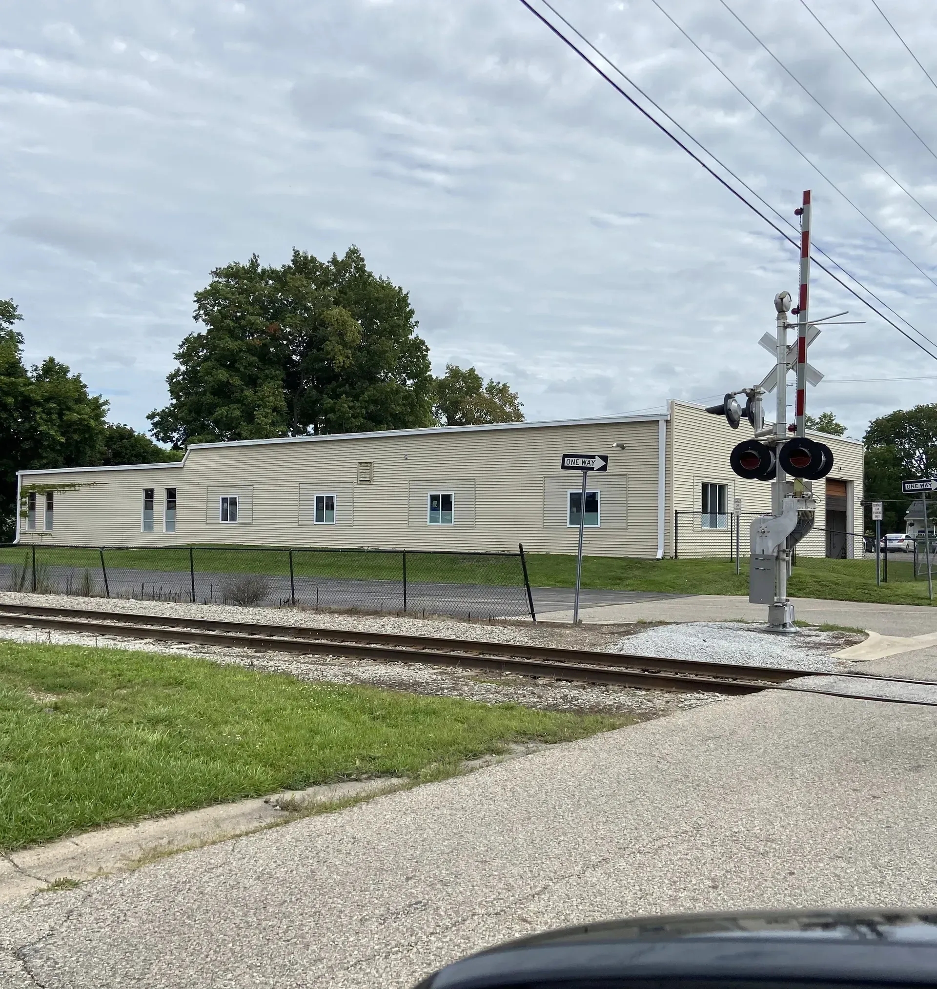 Railroad crossing beside a tan building with black signal lights and cloudy sky