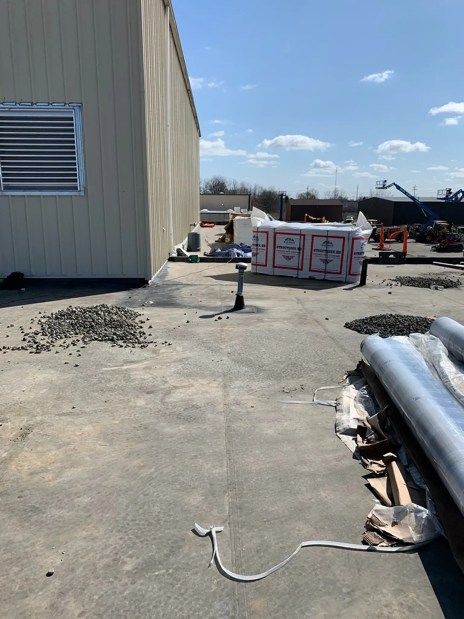 Construction site beside a white building with insulation stacks, scattered debris, and a clear sky.