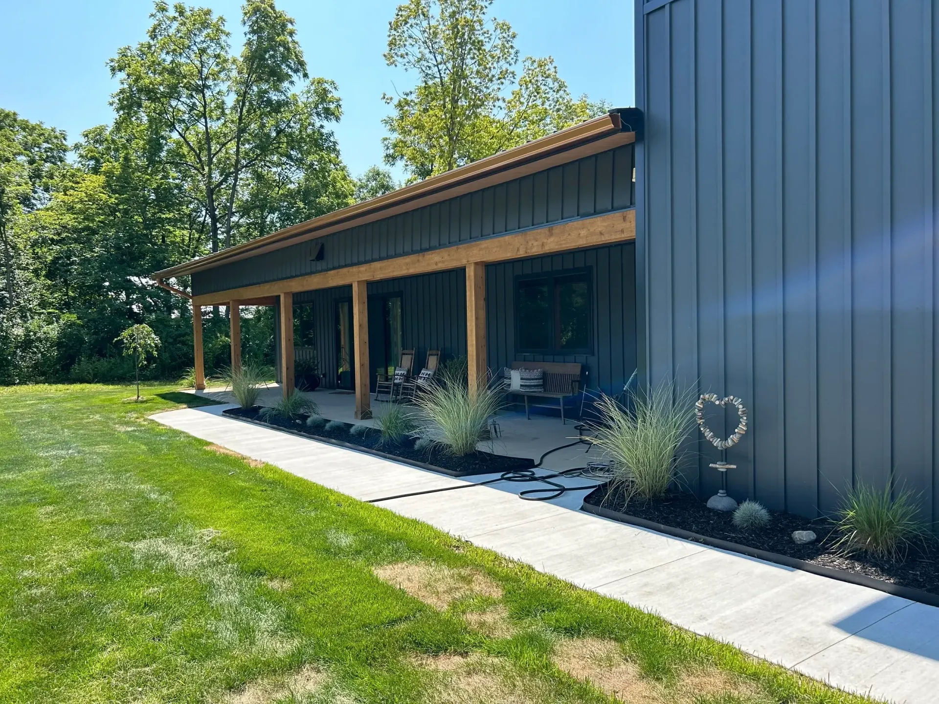 Modern building with a covered porch, blue siding, and a concrete walkway beside a green lawn.