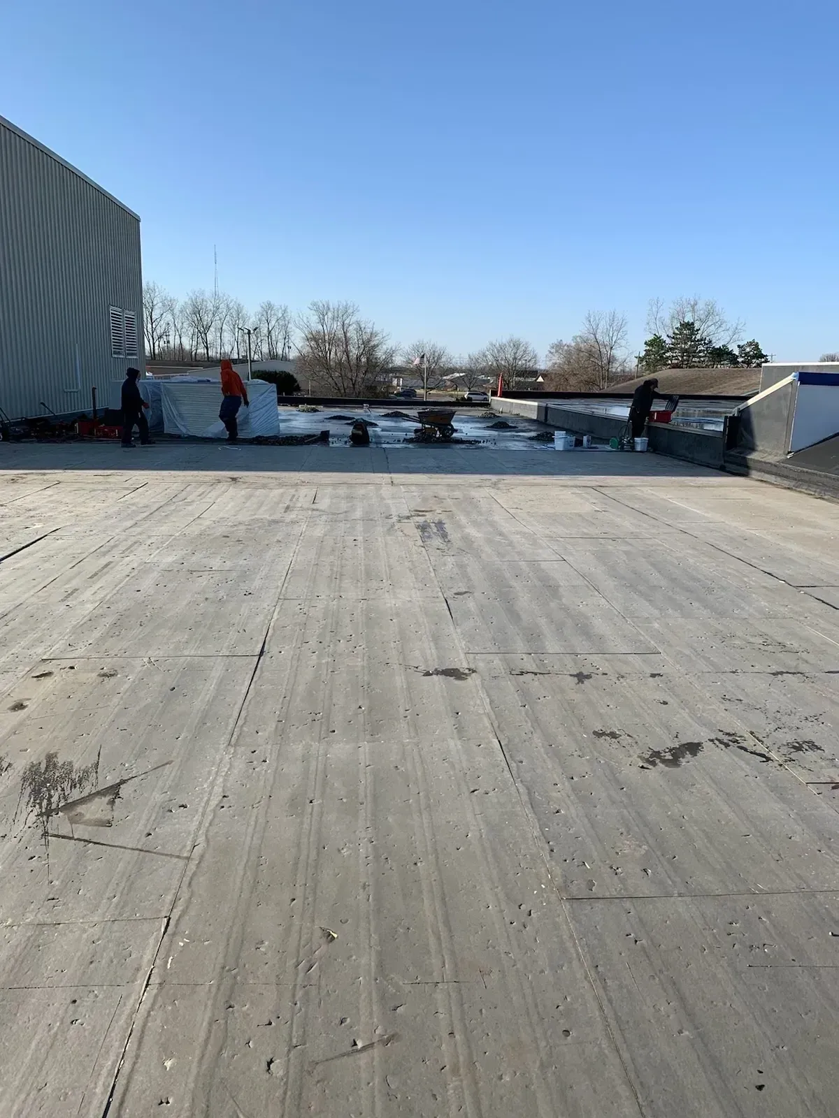 Rooftop with people near HVAC units under a clear blue sky, viewed across a wide concrete surface