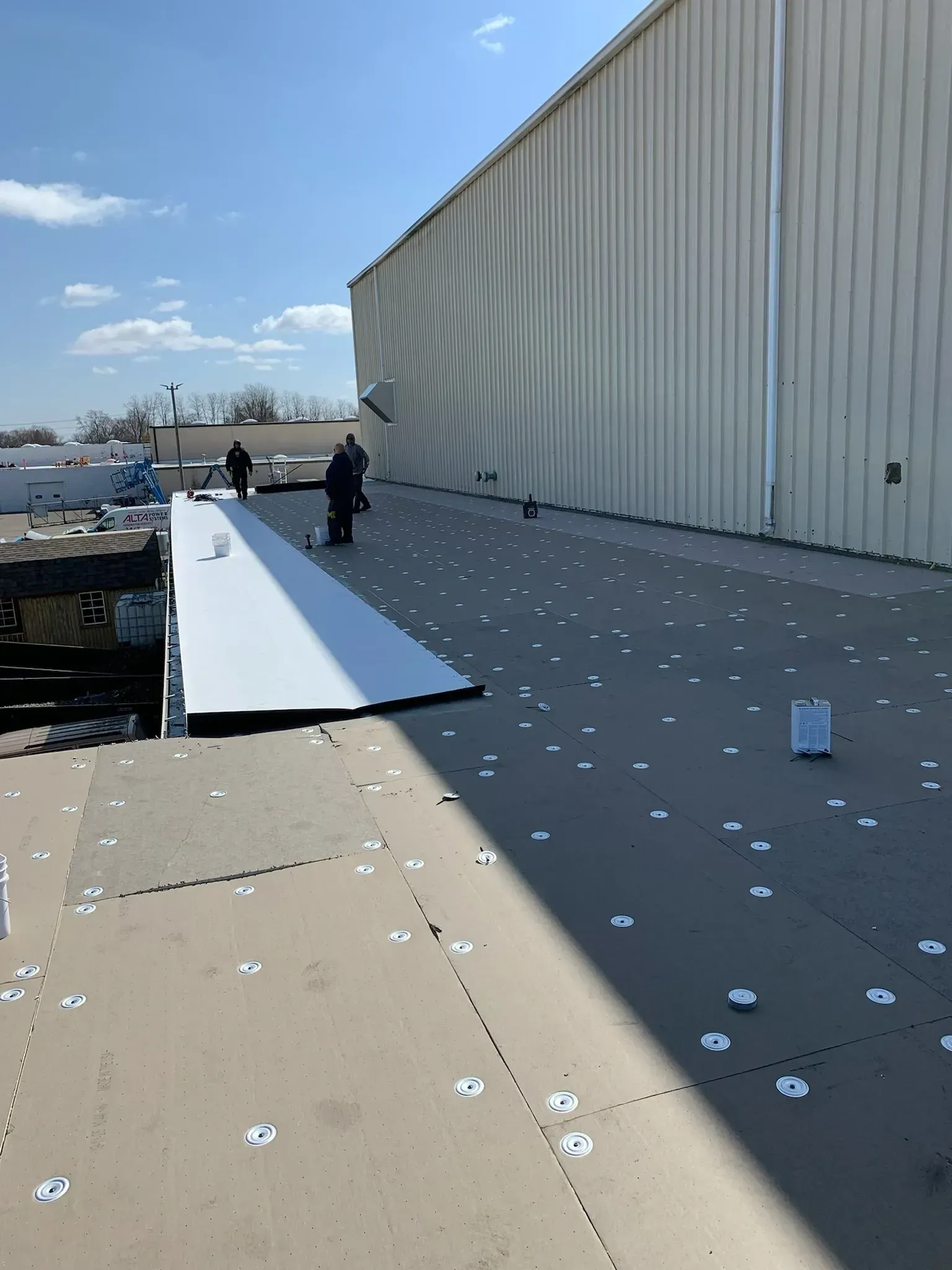 Wind-damaged rooftop with scattered debris and two workers near a large white building.