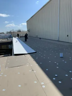 Wind-damaged rooftop with scattered debris and two workers near a large white building.