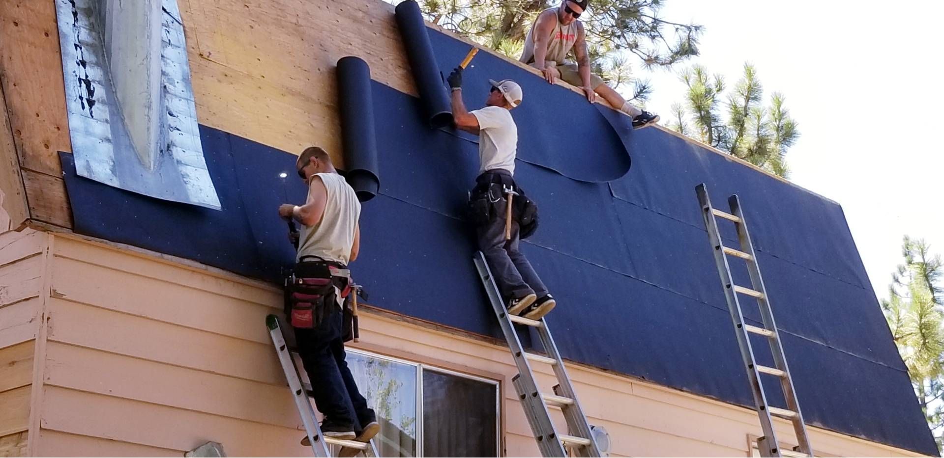 Two workers painting a house exterior blue, with ladders and tarps on the roofline