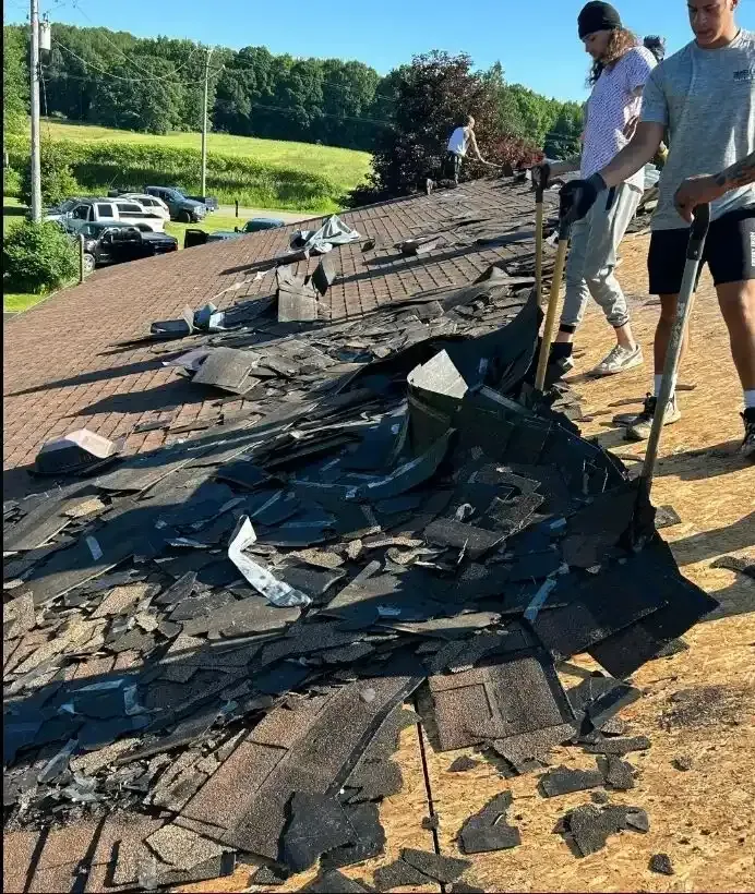 Damaged roof shingles strewn across a roof while two workers inspect the damage outdoors.