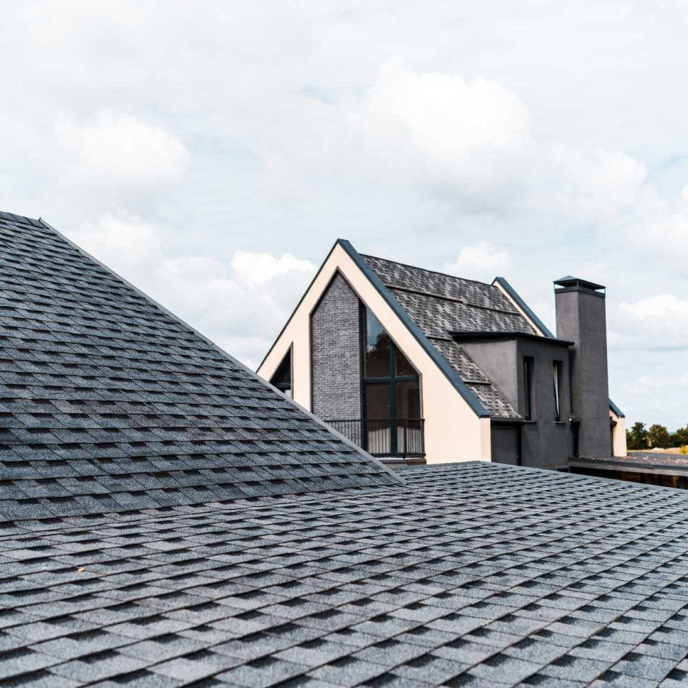 Gabled house roofs with gray shingles under a cloudy sky